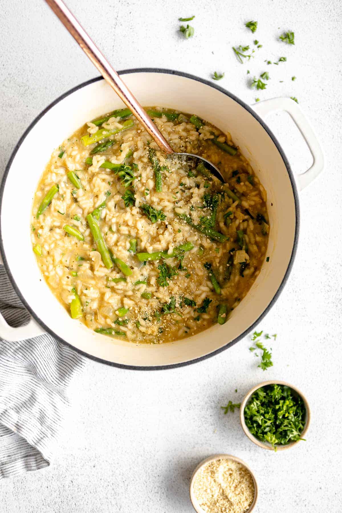 vegan risotto in a pot with a spoon and herbs on the side