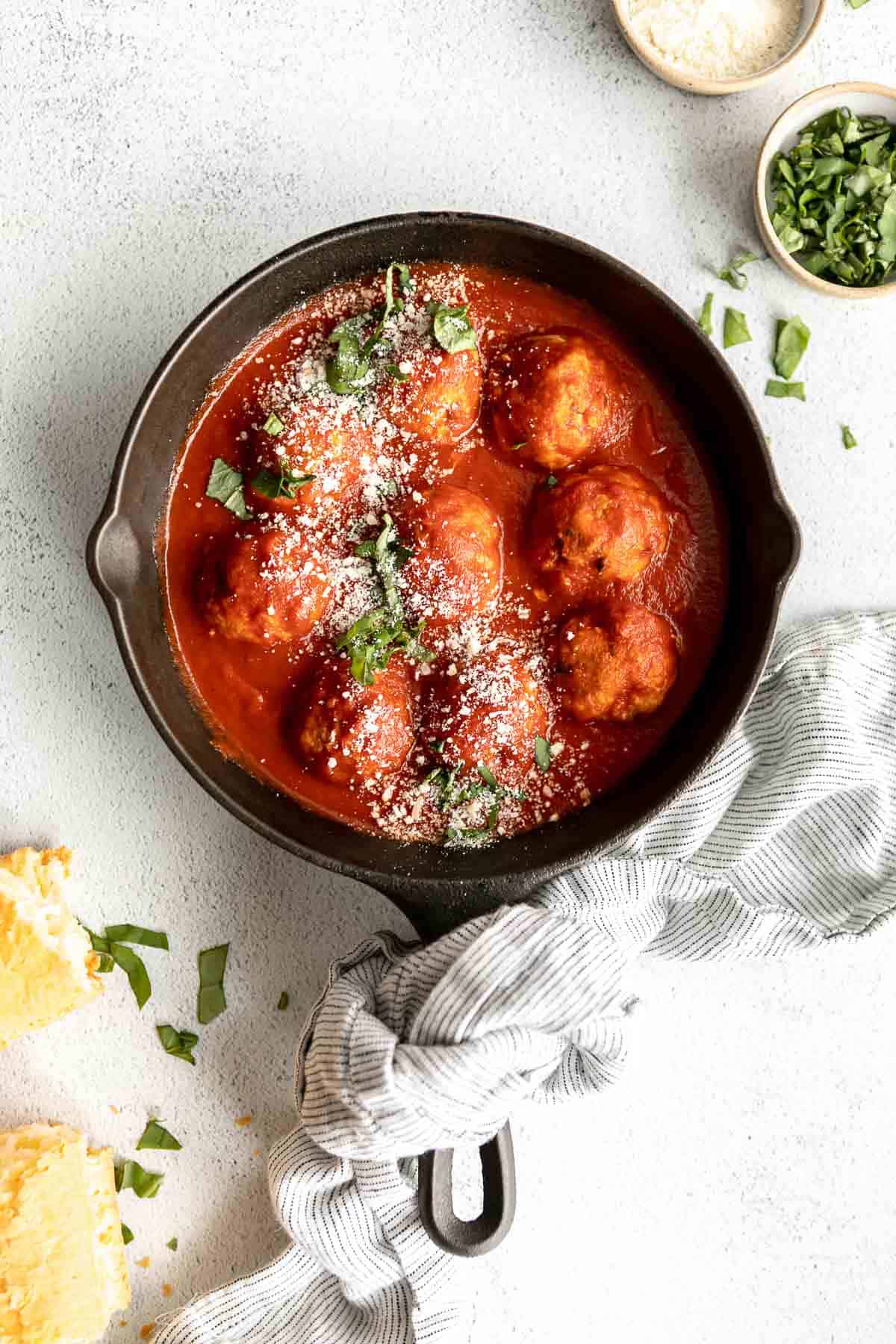 gluten free meatballs in a skillet with parmesan and fresh basil.