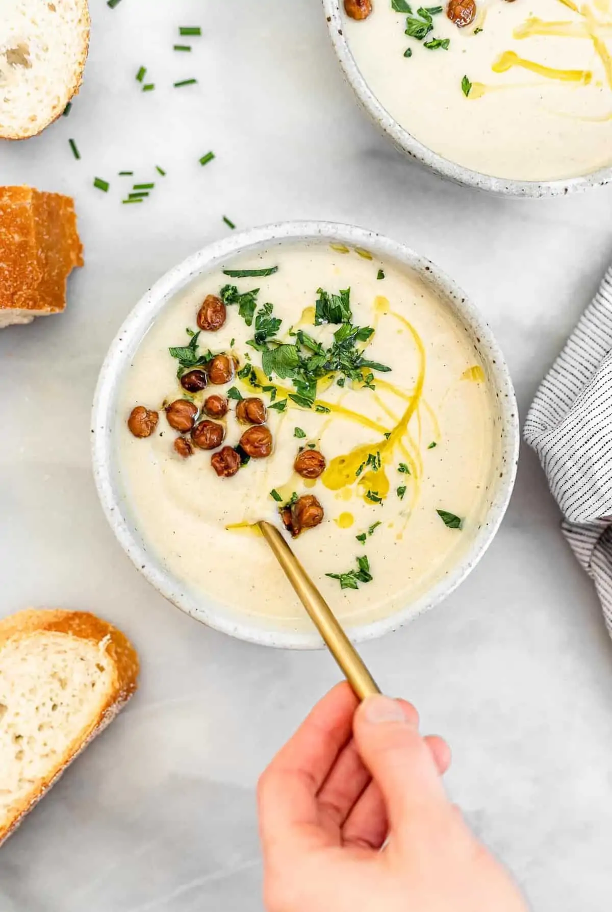 Hand holding a spoon in the bowl of cauliflower soup.
