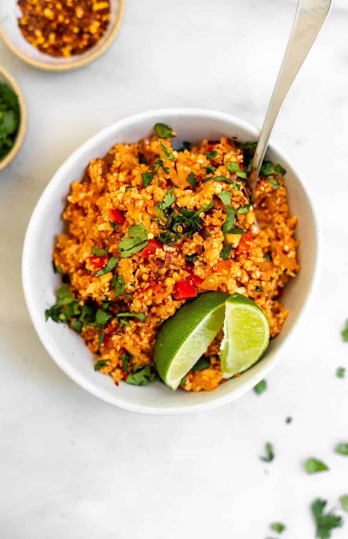Mexican cauliflower rice in a bowl with red pepper flakes on the side.