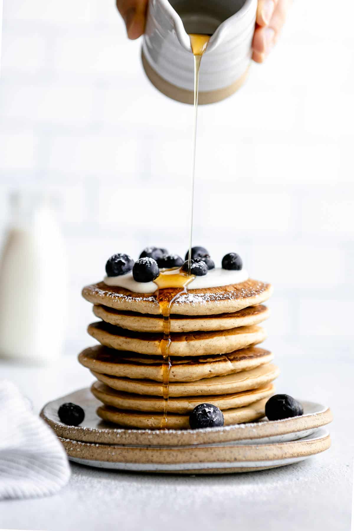 Two plates stacked with oat flour pancakes with maple syrup on top.