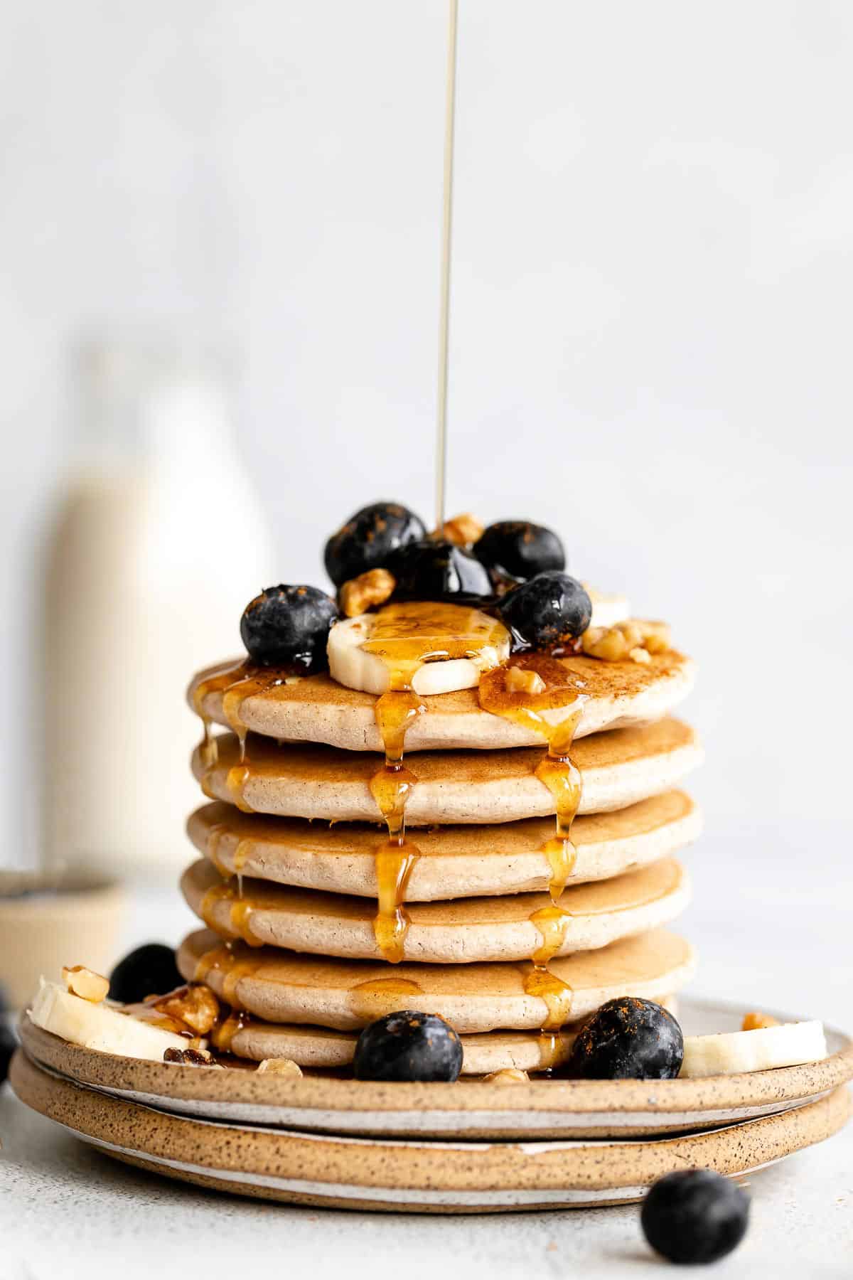 Vegan buckwheat pancakes with blueberries on top and maple syrup pouring down.