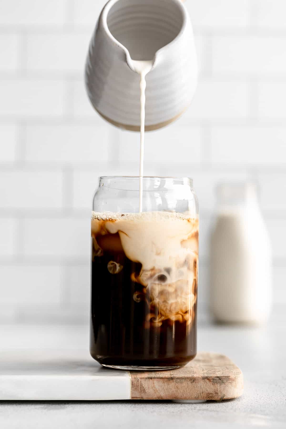 pouring the homemade walnut milk in a cup of iced coffee