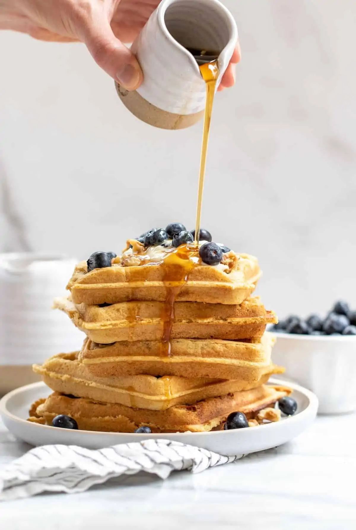Pouring maple syrup on a stack of waffles.