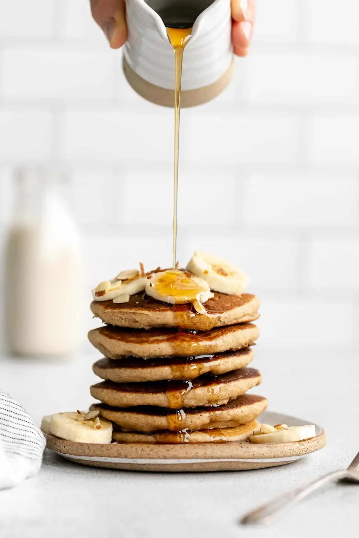 pouring maple syrup over the gluten free banana pancakes