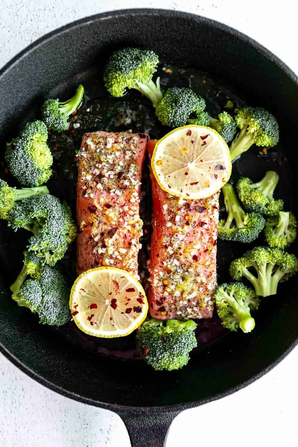salmon fillets in a pan with broccoli and lemon wedges