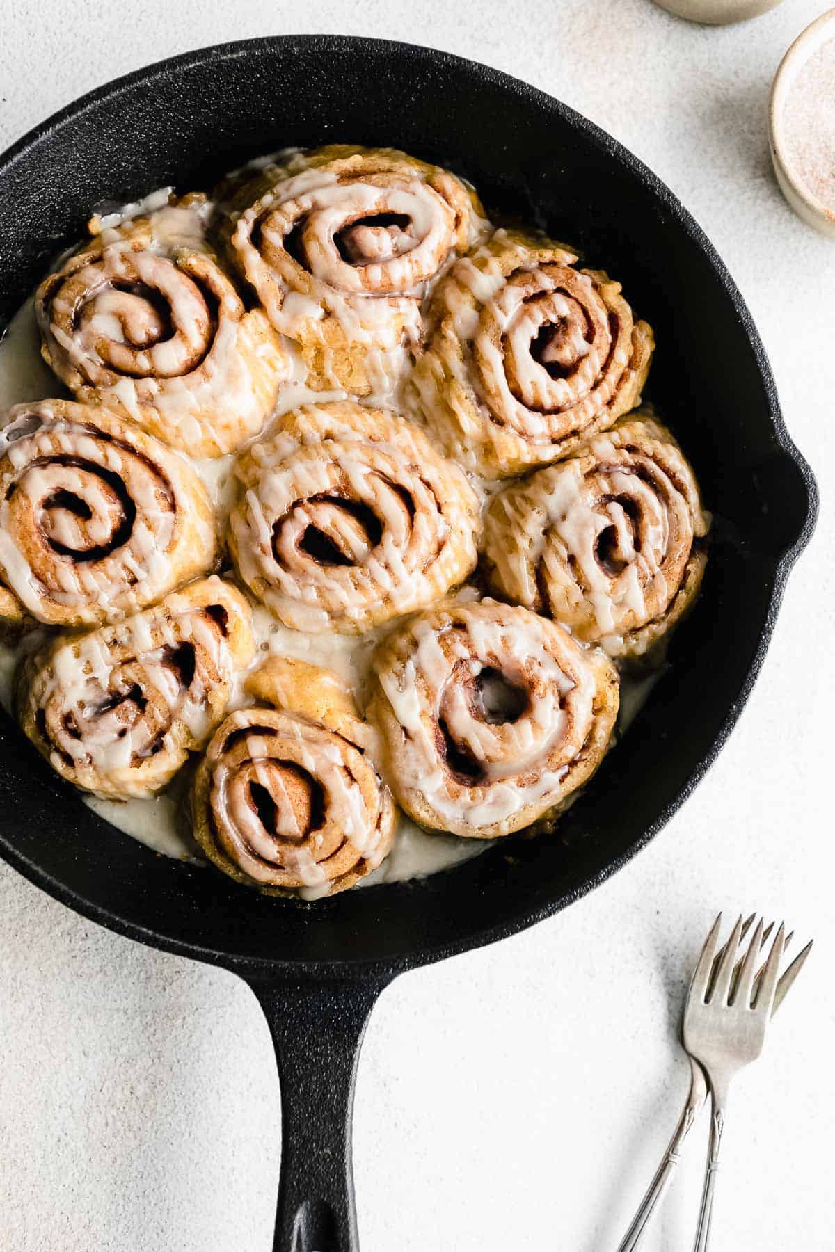 gluten free cinnamon buns in a cast iron skillet with drizzle of icing