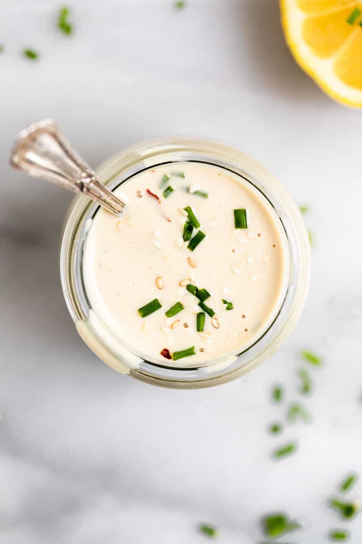 Tahini dressing in a glass jar with lemon wedges on the side.