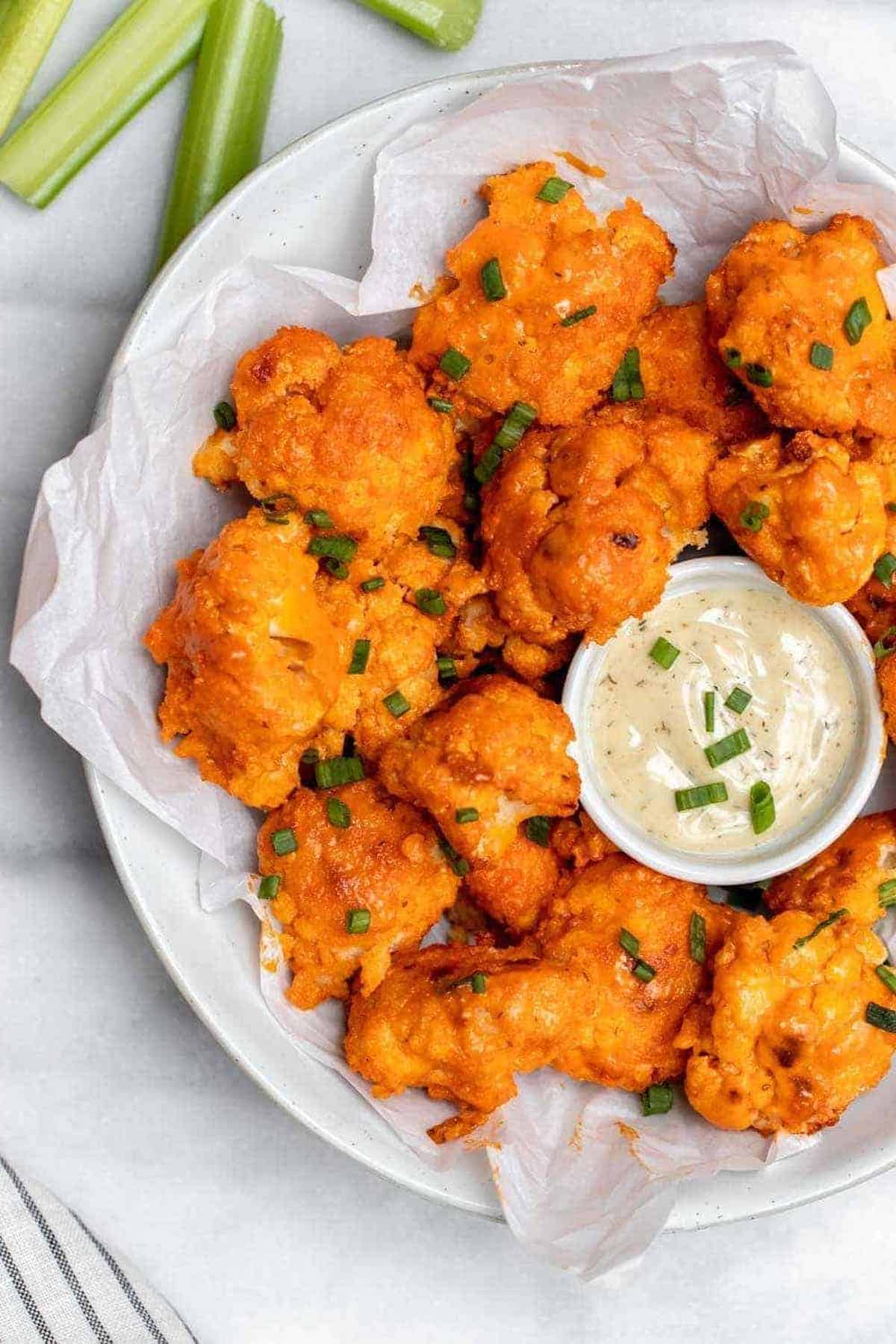 Baked buffalo cauliflower with chives on top in a large bowl. 