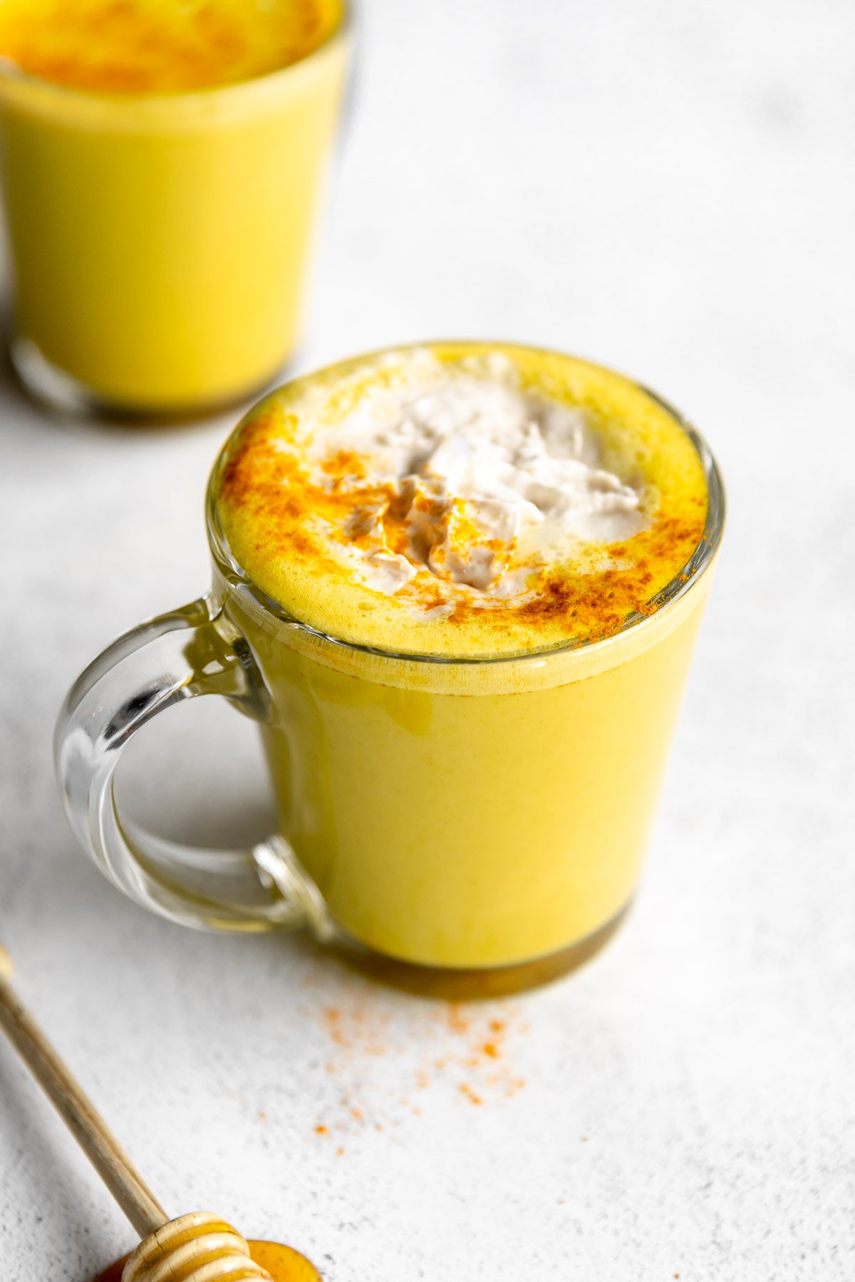 golden milk turmeric latte in a cup with whipped cream on top and honey