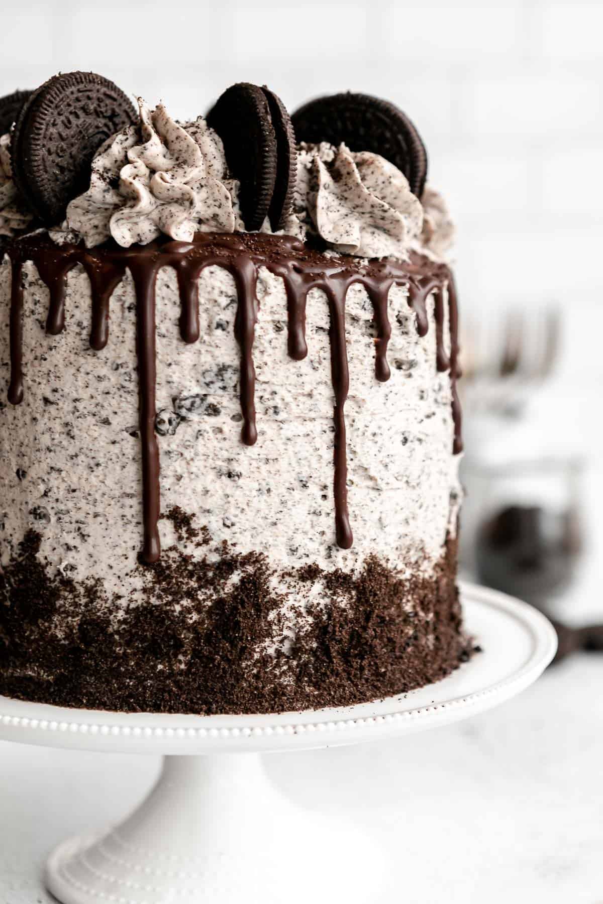 oreo cake on a cake stand with chocolate ganache drip down the side