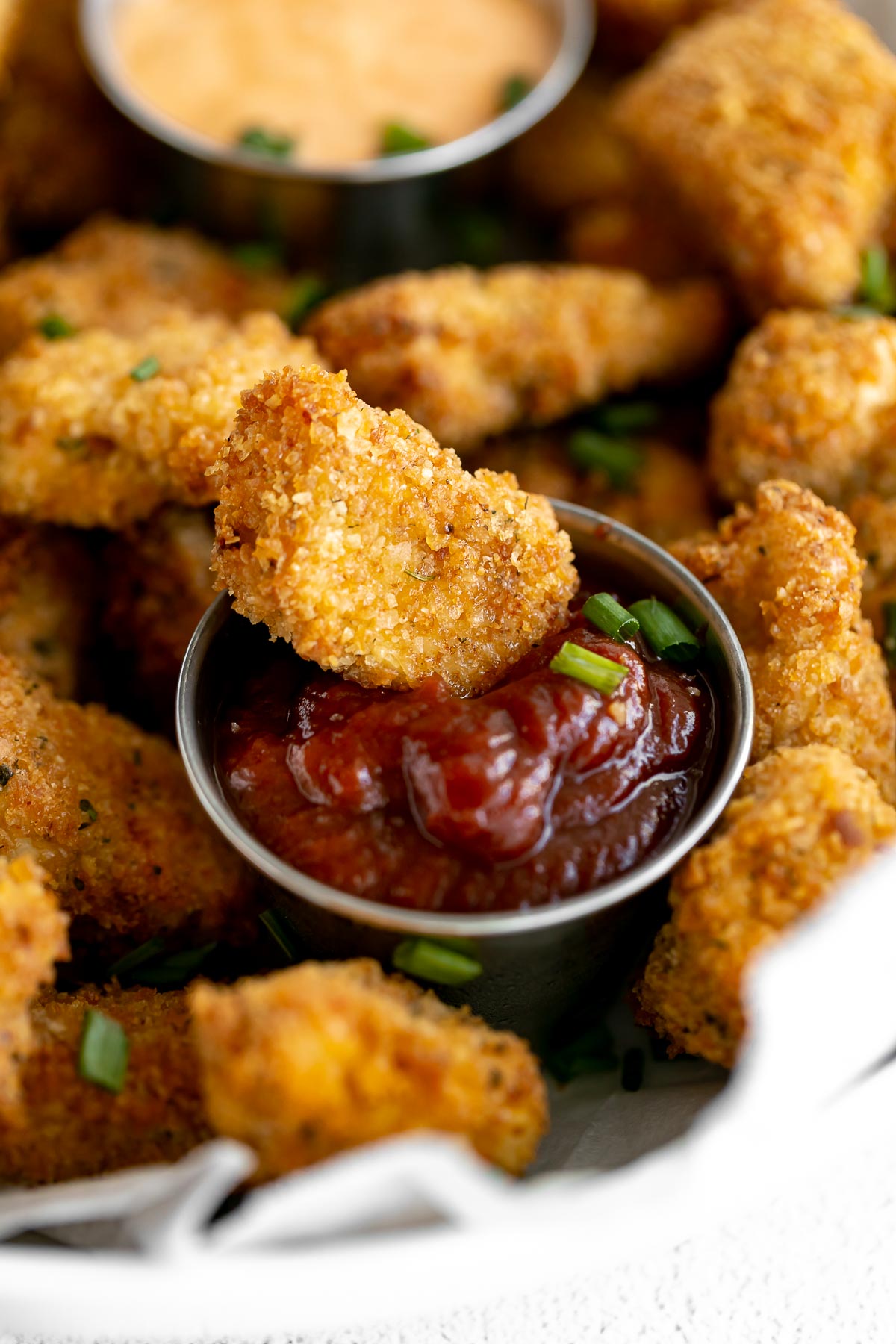Healthy chicken nugget in a bowl of ketchup with chives.