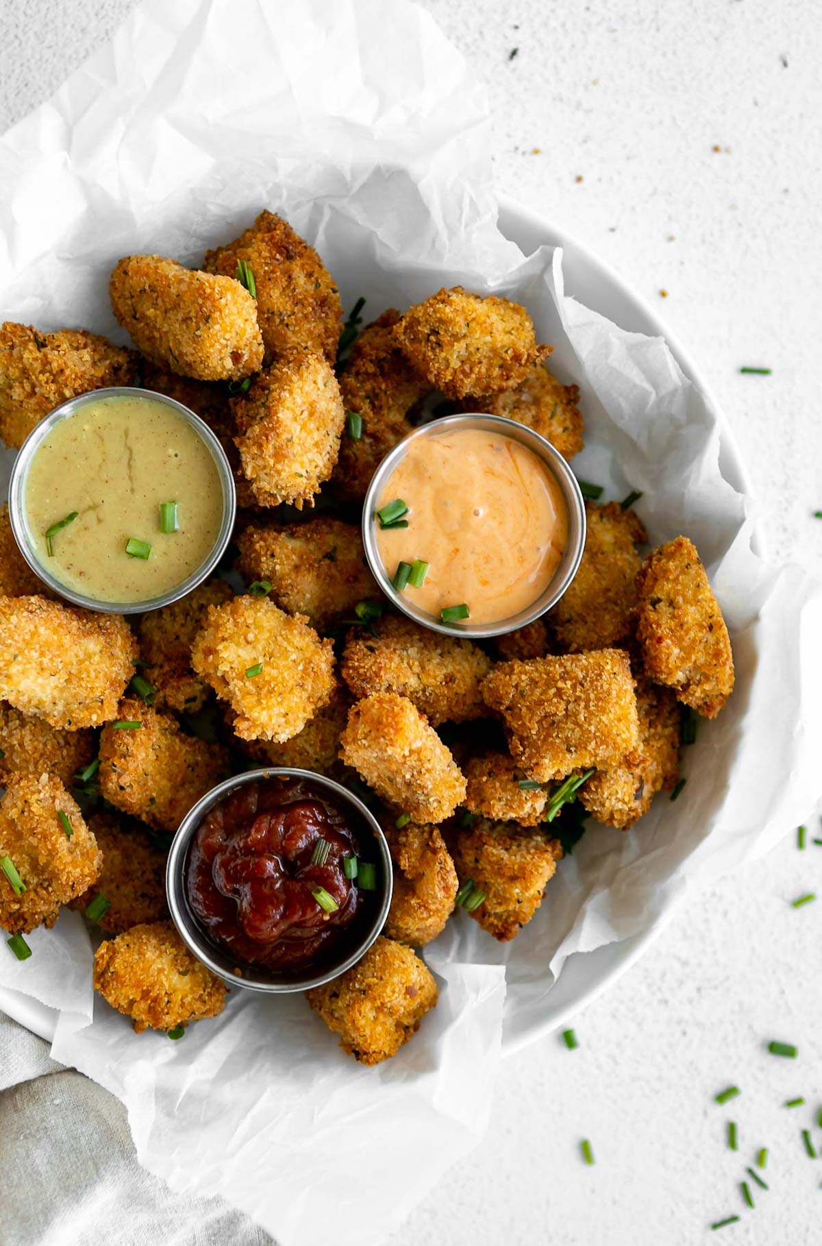 Air fryer chicken nuggets in a bowl with three dipping sauces.