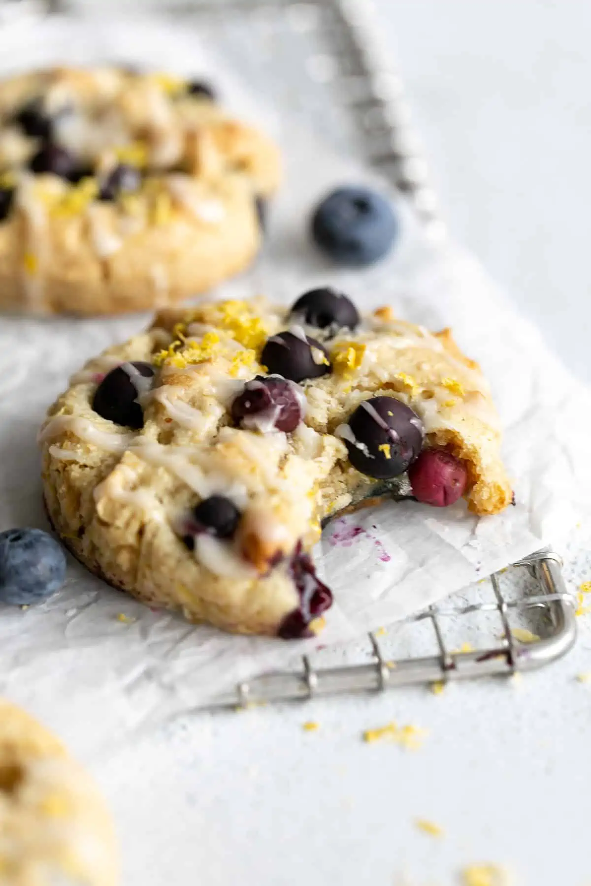 three vegan lemon cookies on a wire rack with blueberries and lemon zest