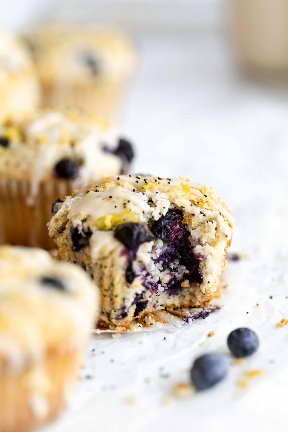 gluten free blueberry muffin on parchment paper with a bite taken out with lemon zest