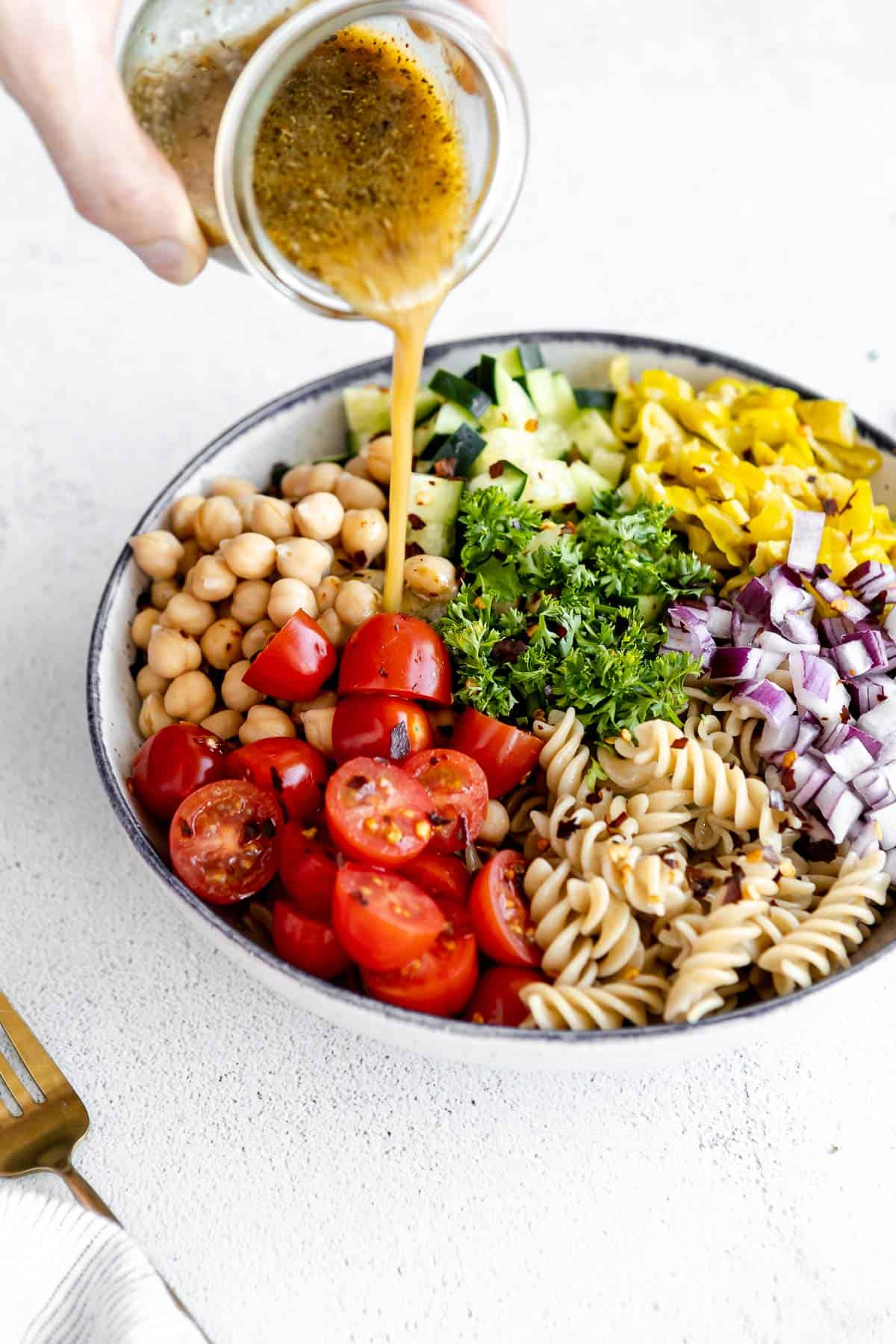 pouring the dressing on top of the vegan chickpea pasta salad