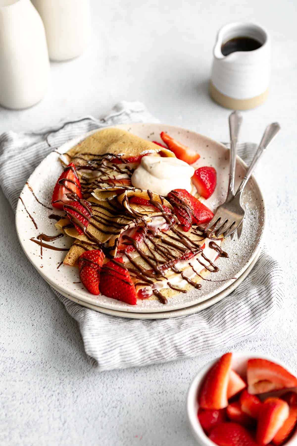 gluten free crepes on a plate with strawberries, whipped cream and a drizzle of chocolate