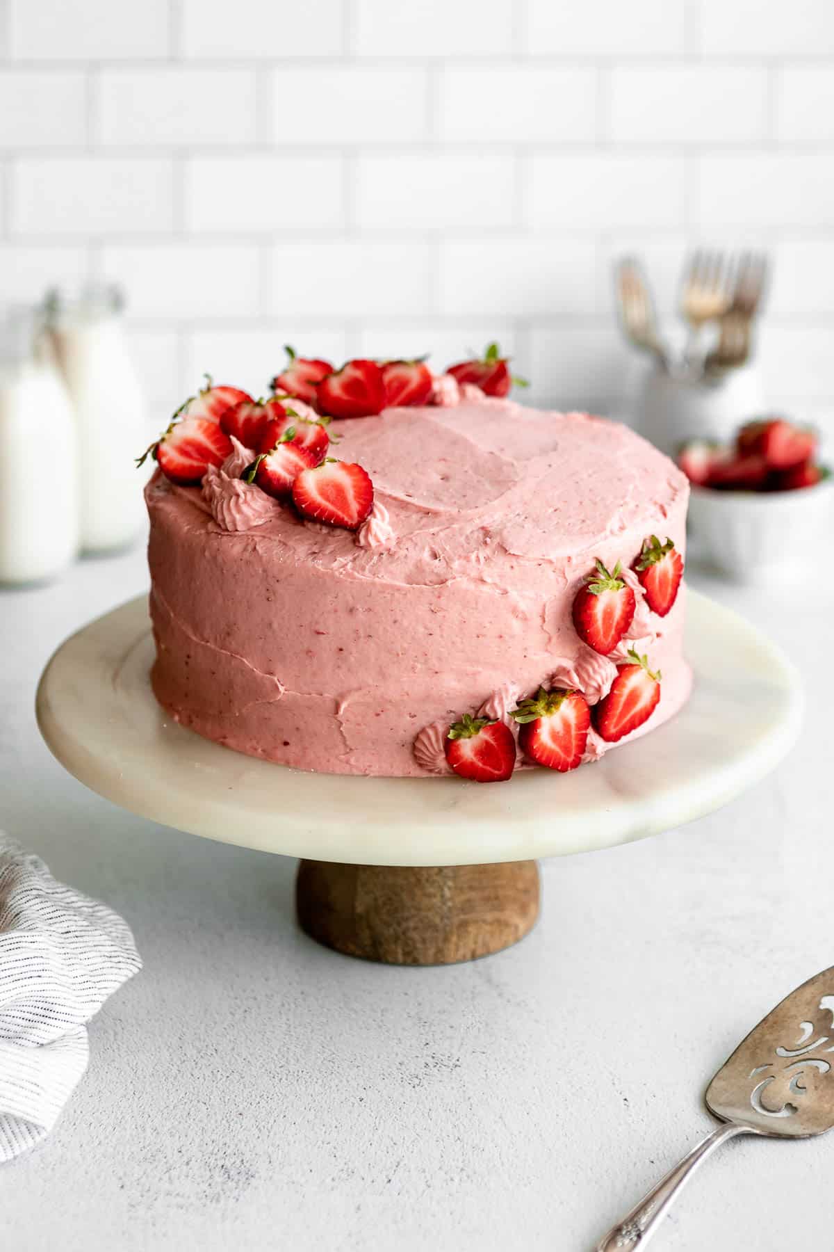 gluten free strawberry cake with jars of milk in the background on a white board