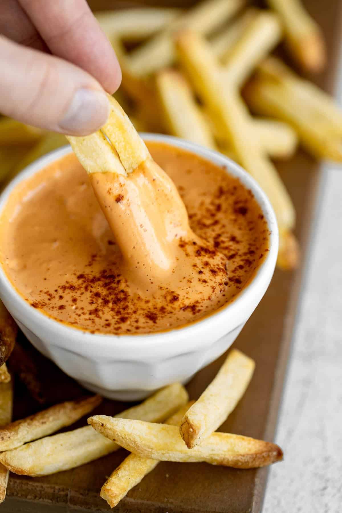 dipping two french fries into the vegan chipotle aioli in a white bowl