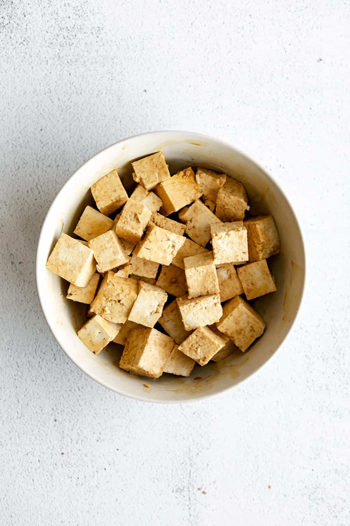 tofu cut into cubes marinating in a bowl