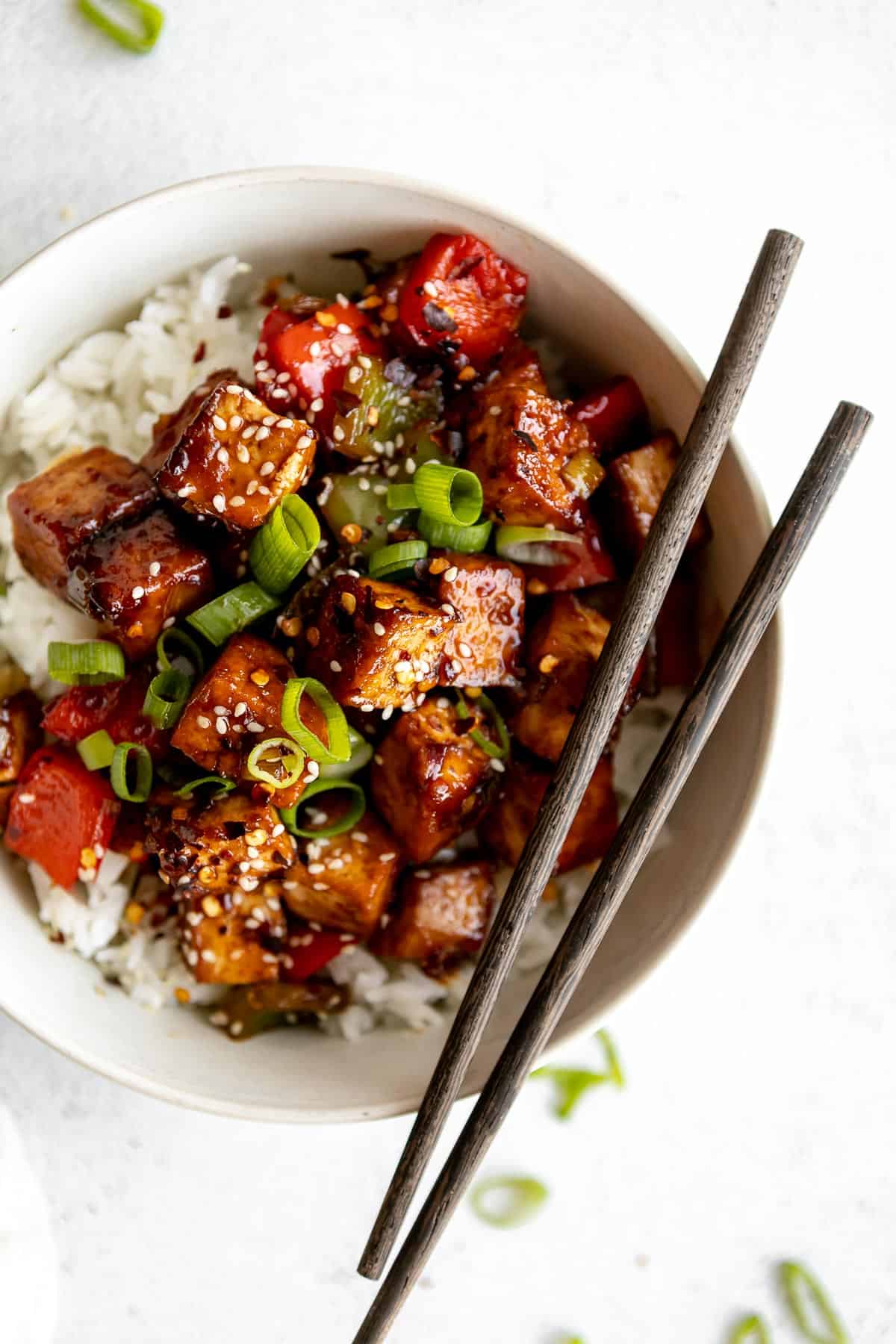 kung pao tofu in a white bowl over white rice with brown chopsticks