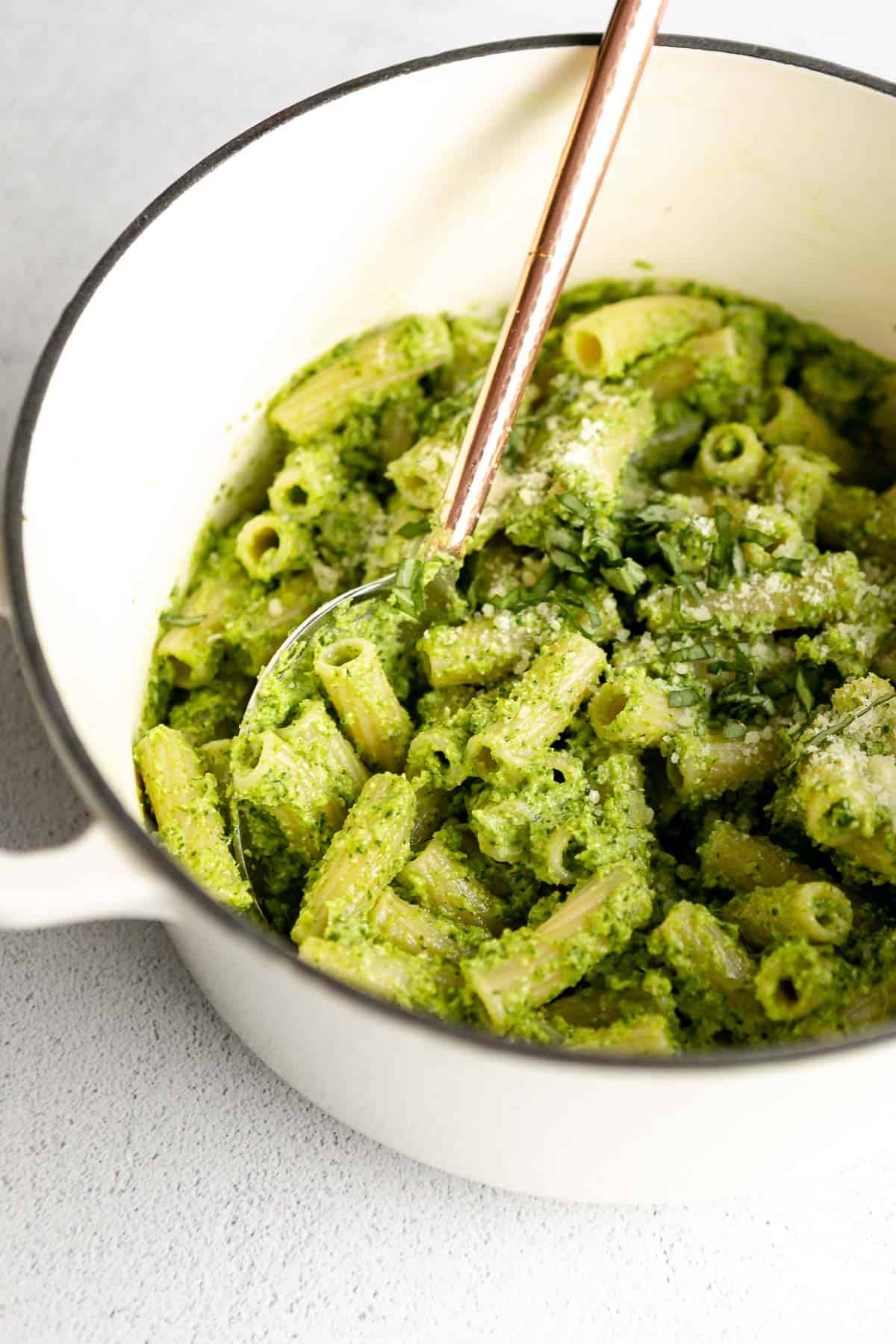 broccoli pesto pasta in a white pot with a spoon on the side