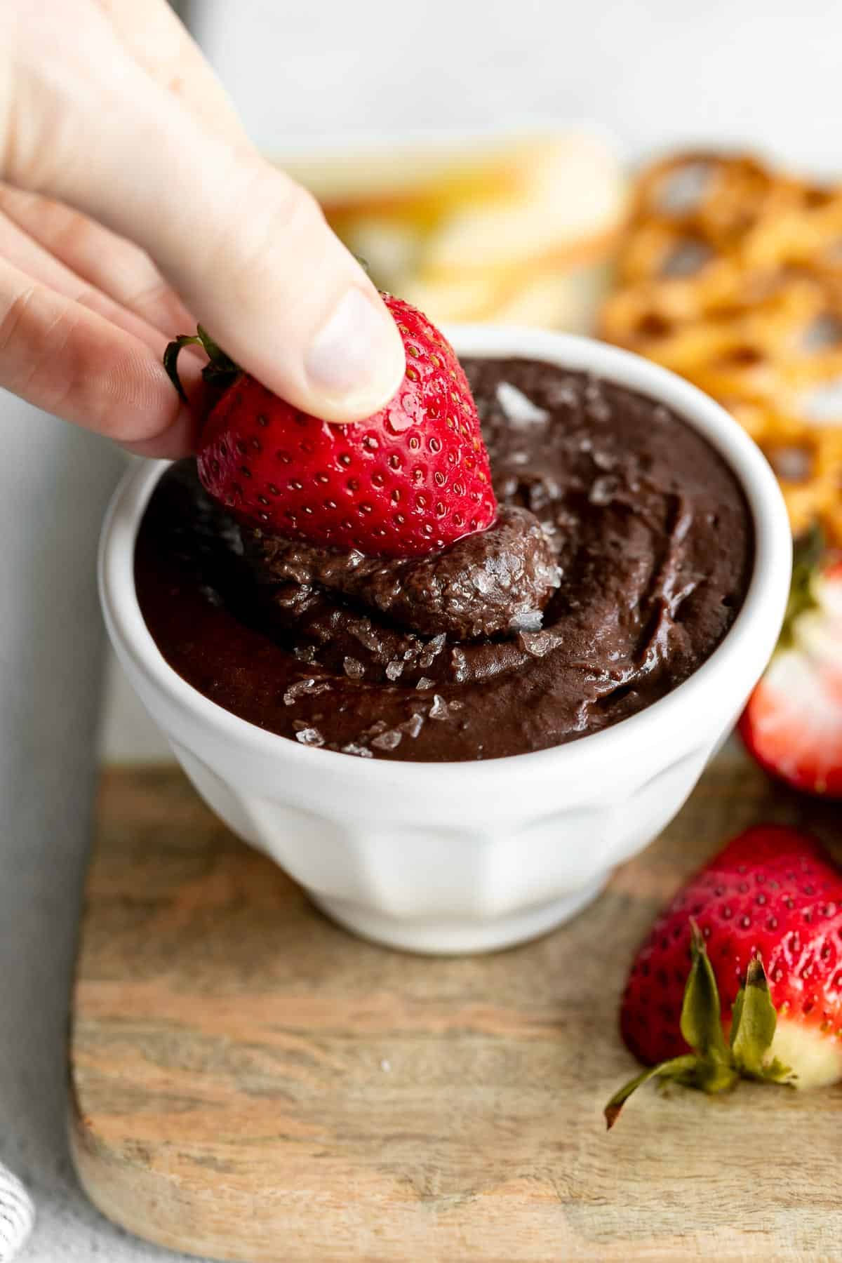 chocolate brownie batter dessert hummus in a white bowl with a strawberry dipping in
