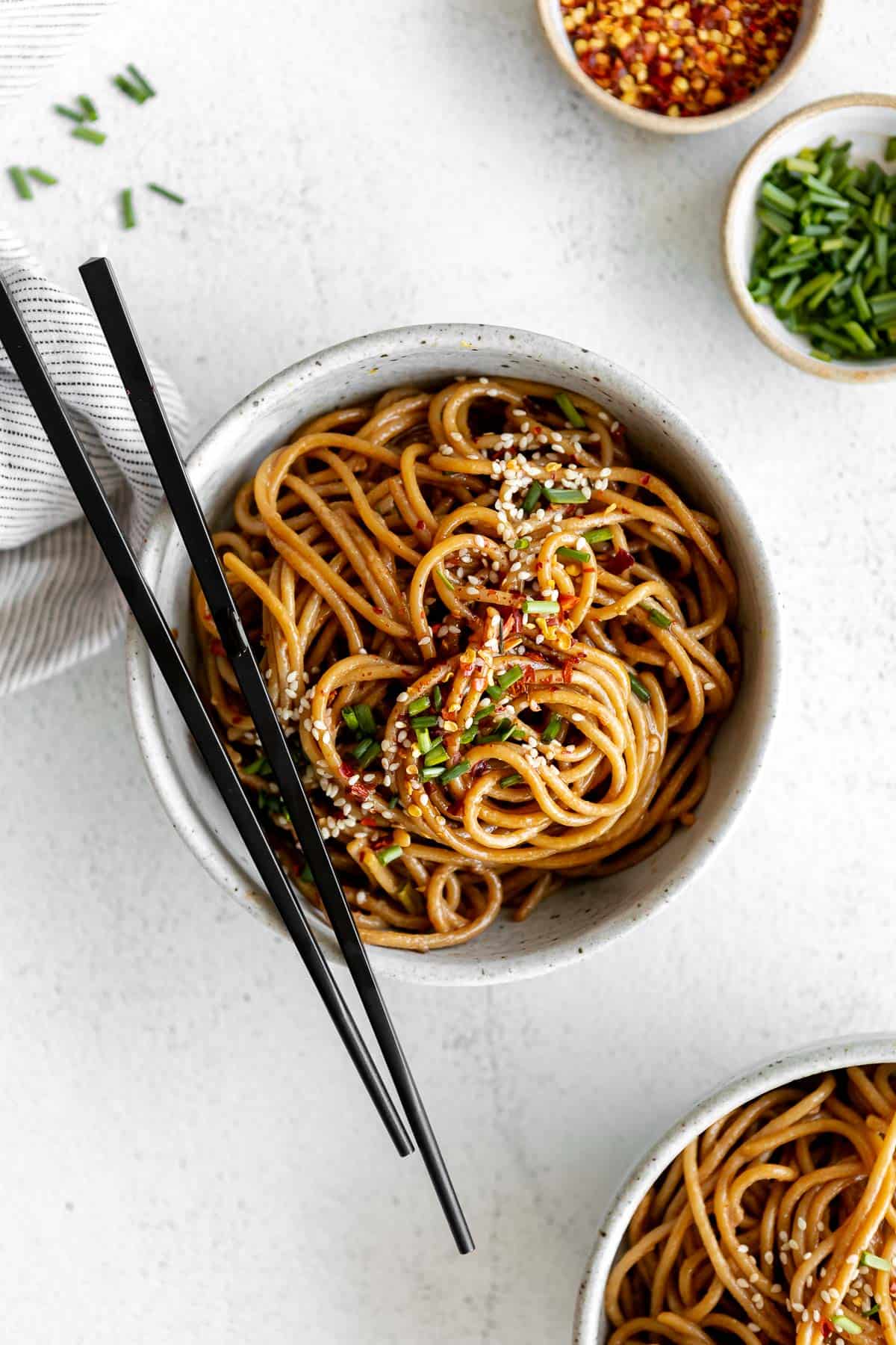 sesame noodles in a bowl with green onion and chopsticks