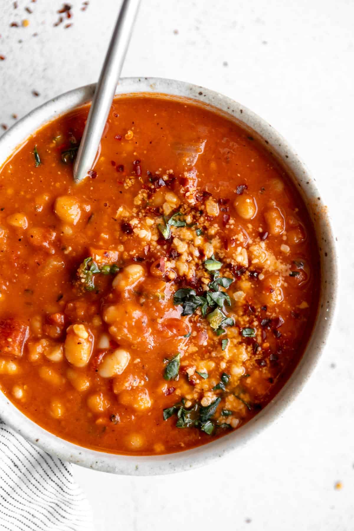 up close image of the vegan white bean tomato soup in a bowl with red pepper flakes on top