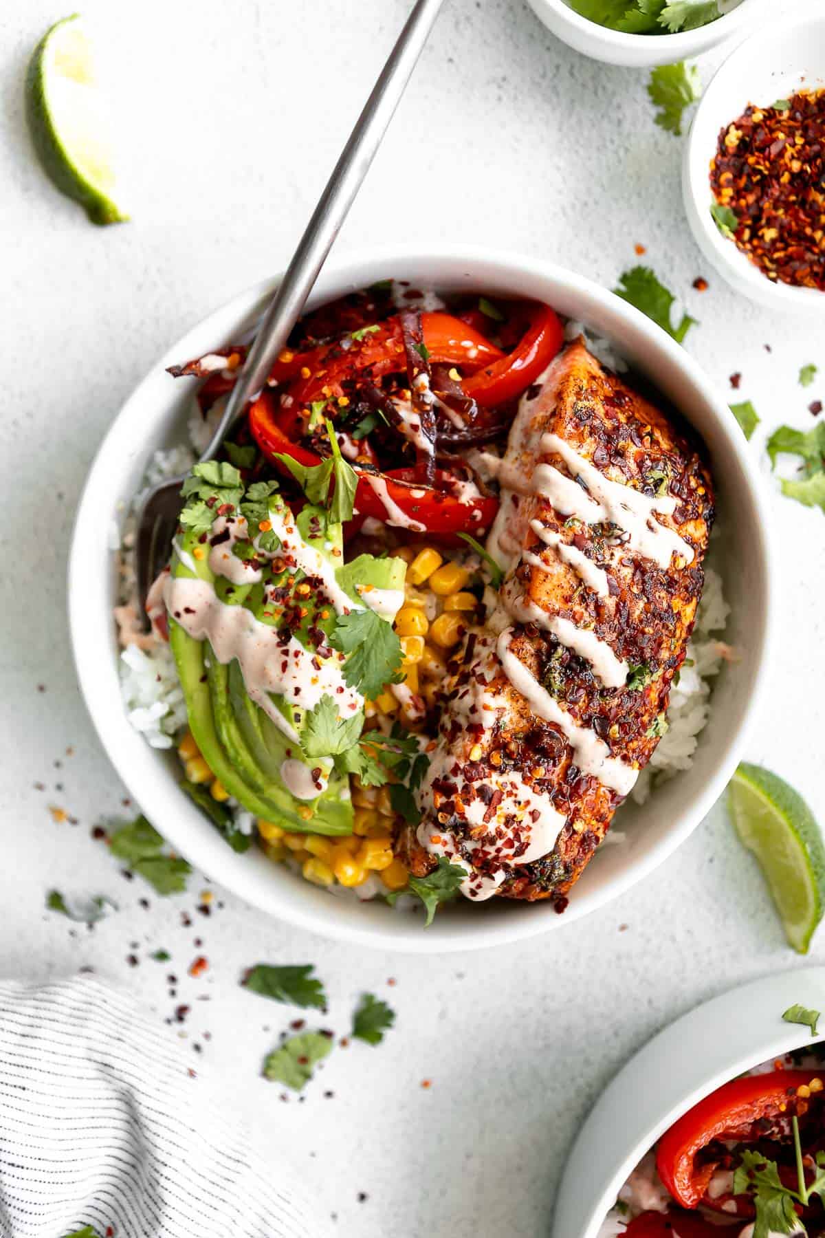 two baked salmon burrito bowls with corn, roasted veggies and avocado