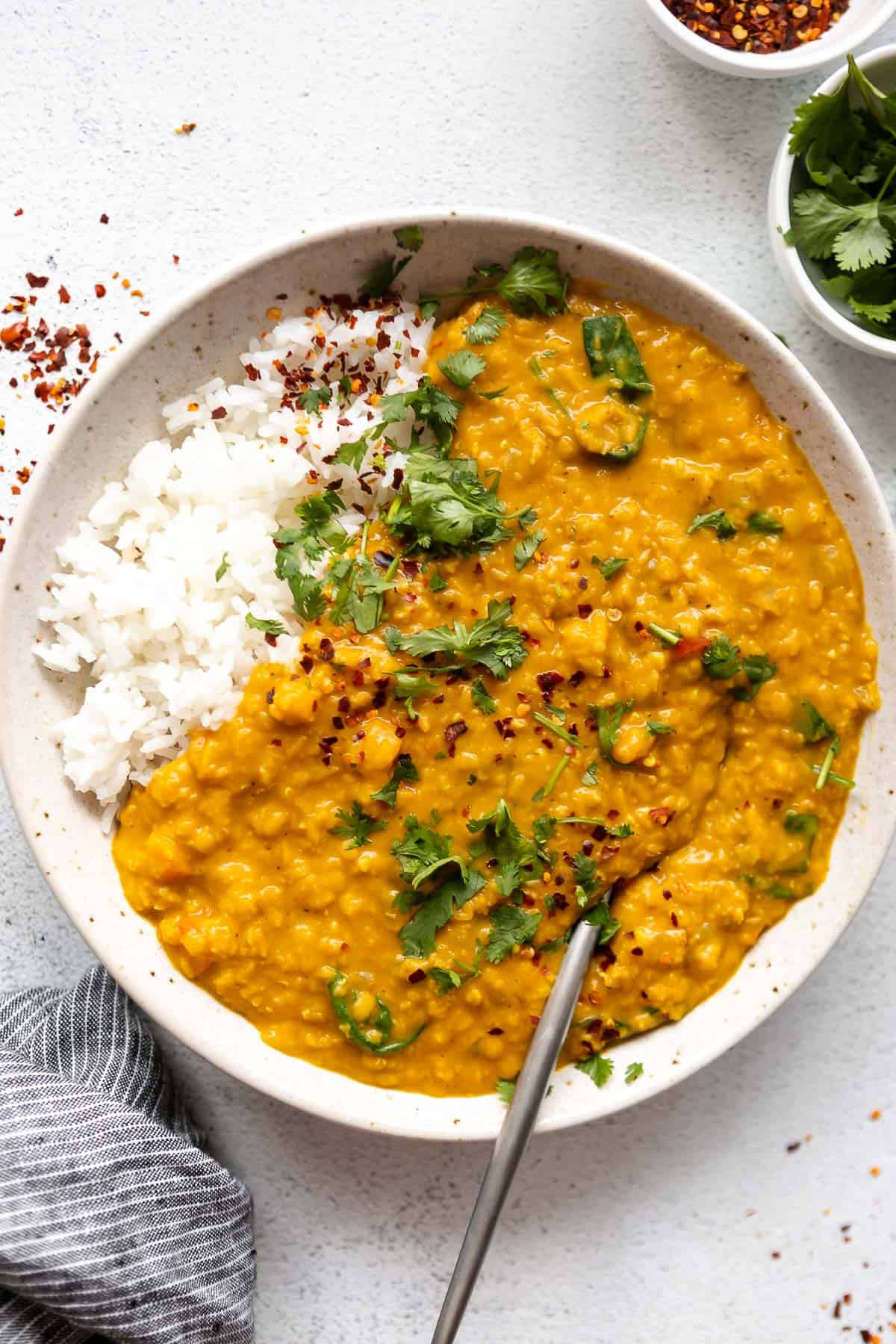 vegan red lentil dahl in a bowl with a spoon on the side