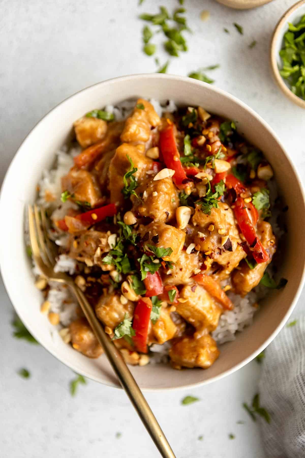 peanut butter chicken in a bowl with cilantro and peanuts on top
