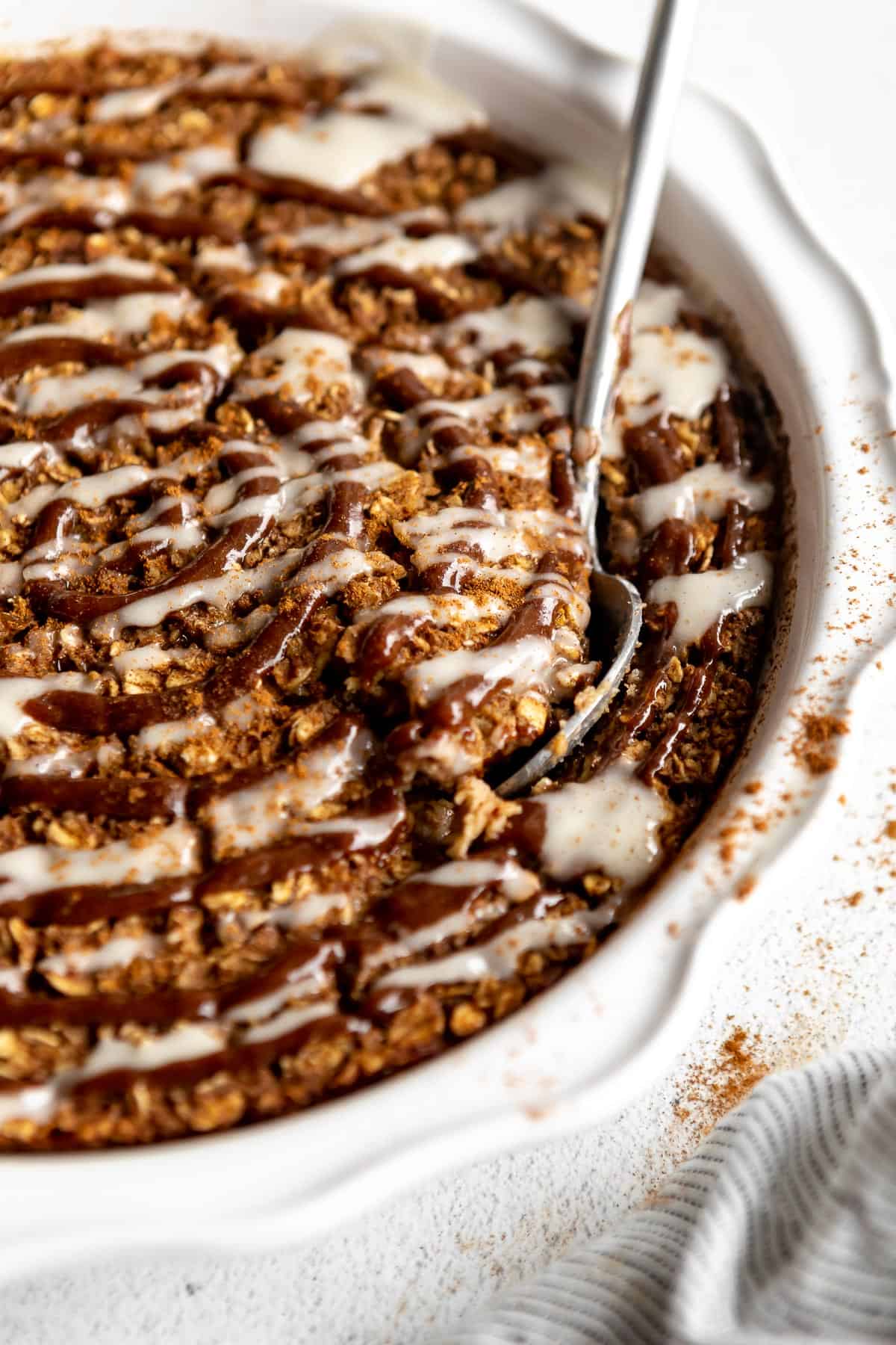 cinnamon roll baked oatmeal in a pie dish with a spoon on the side