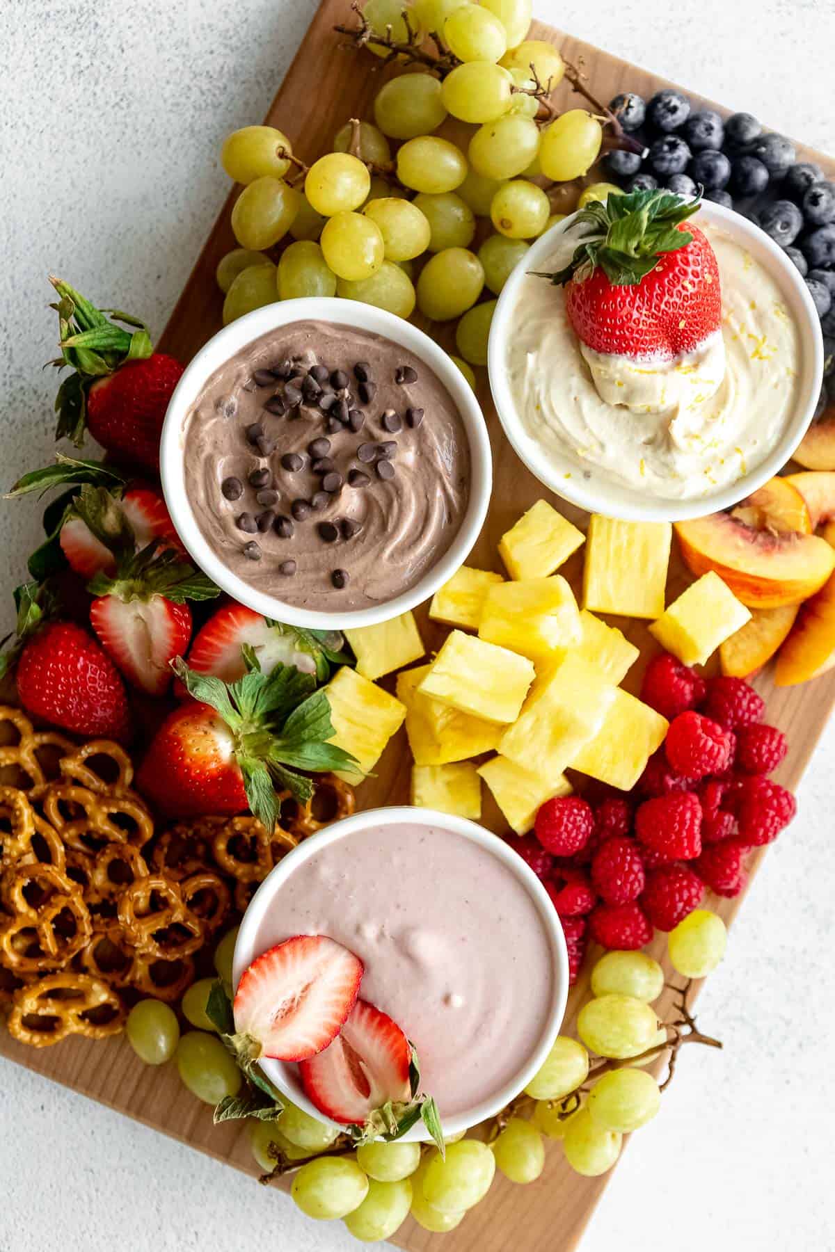 wood board with three fruit dip flavors and pretzels on the side