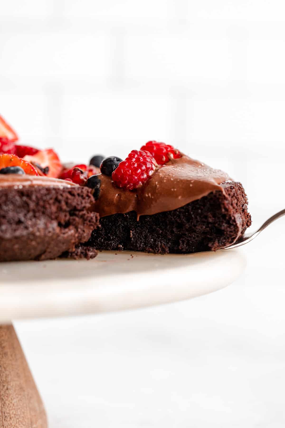 gluten free flourless chocolate cake on a cake stand with a slice pulled out