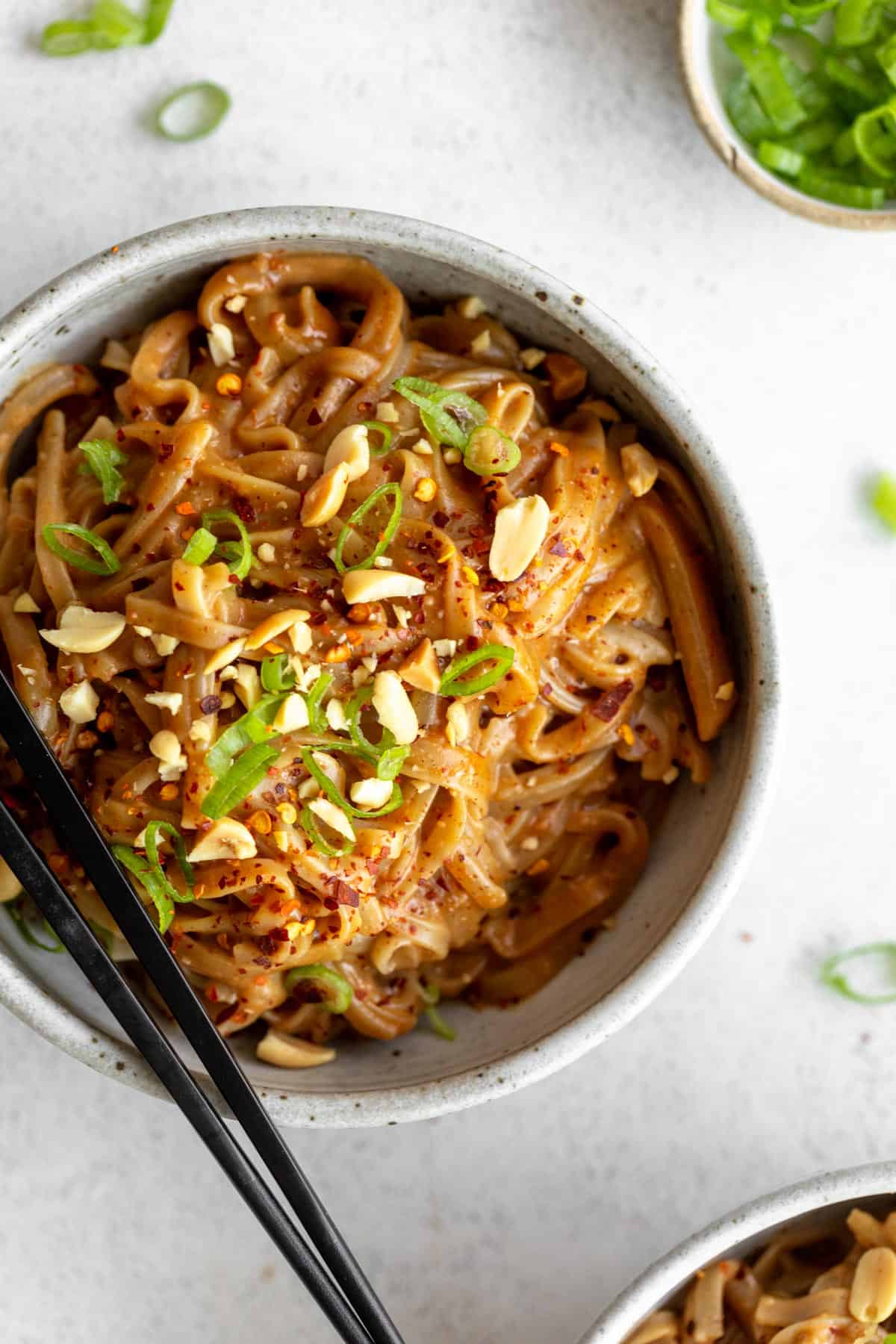 peanut butter noodles in a bowl with spicy peanuts on top