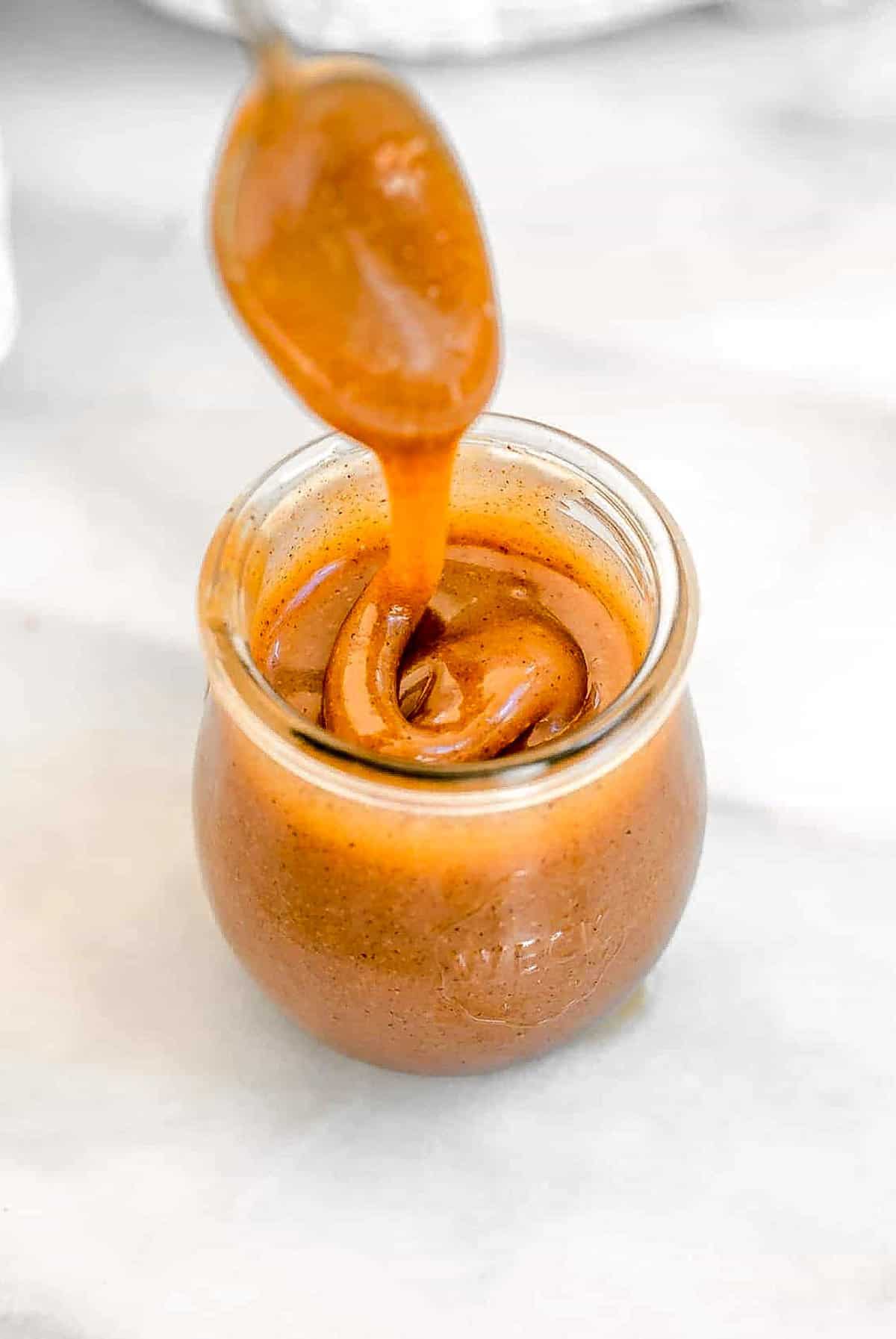 Spoon scooping out the vegan caramel from a glass jar.