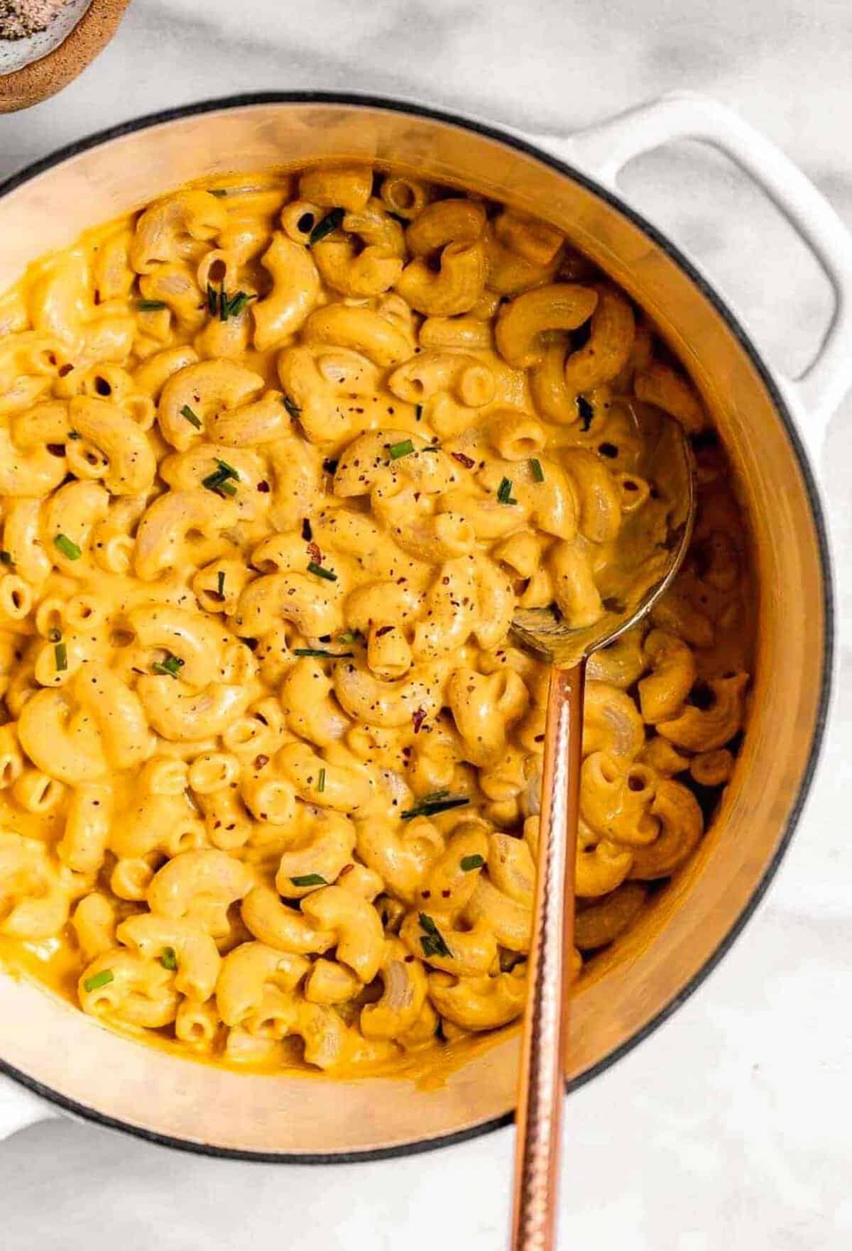 vegan sweet potato mac and cheese in a pot with a spoon on the side