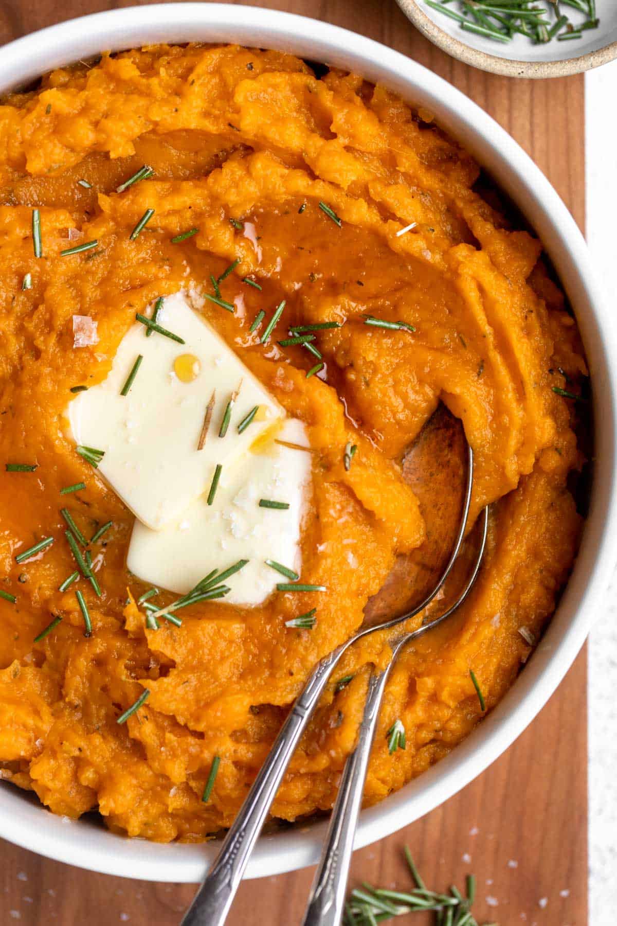 mashed sweet potatoes in a bowl with fresh herbs on top