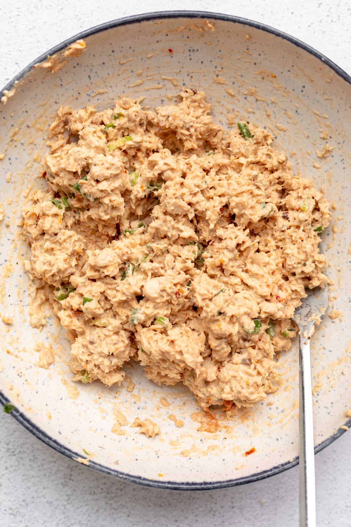 salmon salad in a bowl after mixing with a fork on the side