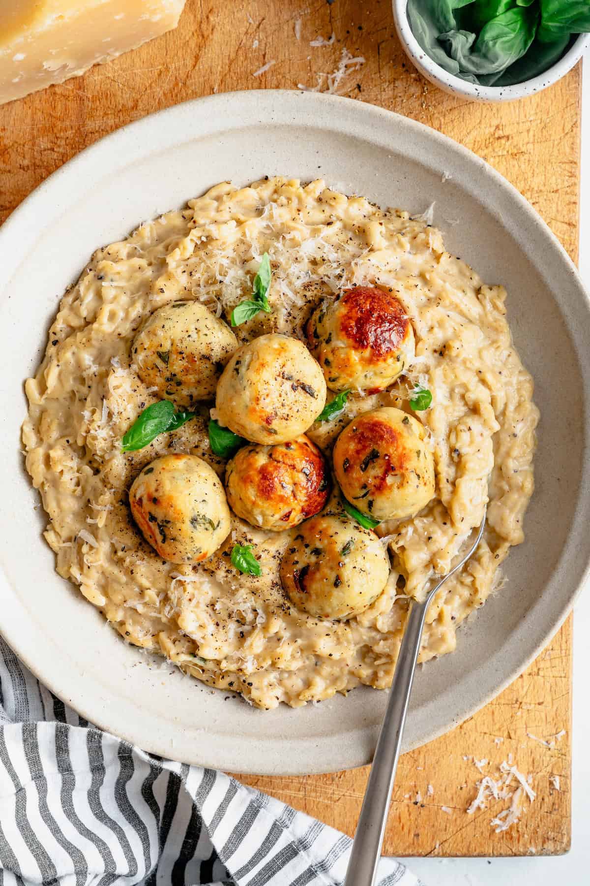 cacio e pepe orzo in a bowl with fresh basil and chicken meatballs on top