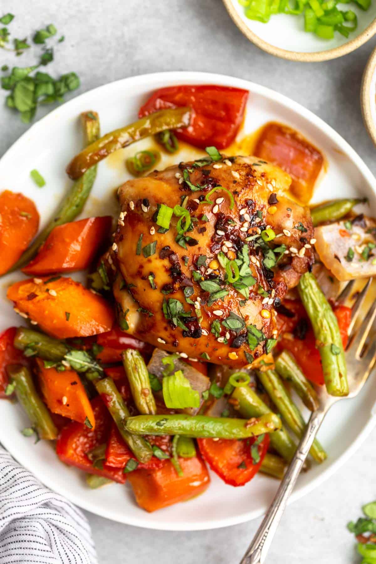 sesame chicken thighs with veggies on a plate with a fork on the side